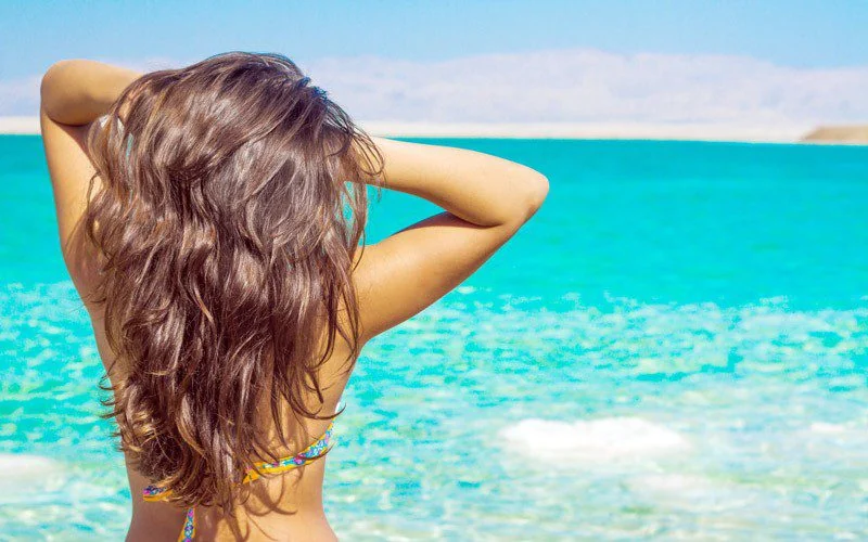 Mulher junto ao mar com cabelo comprido exposto ao sol no verão